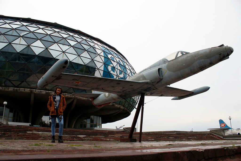 A woman standing in front of the Museum of Aviation in Belgrade, next to a plane